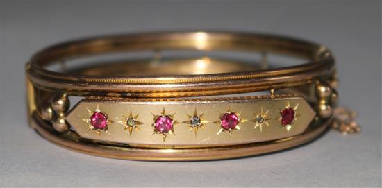 A late Victorian 9ct gold, ruby and diamond set hinged openwork bangle.